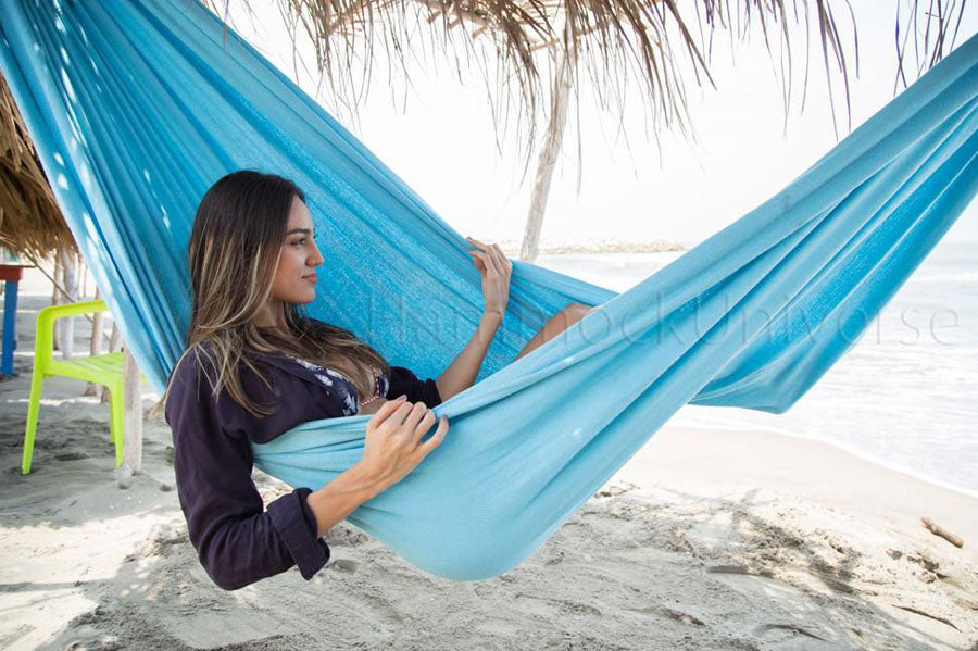 A woman lounging in a Colombian double hammock on a beach.