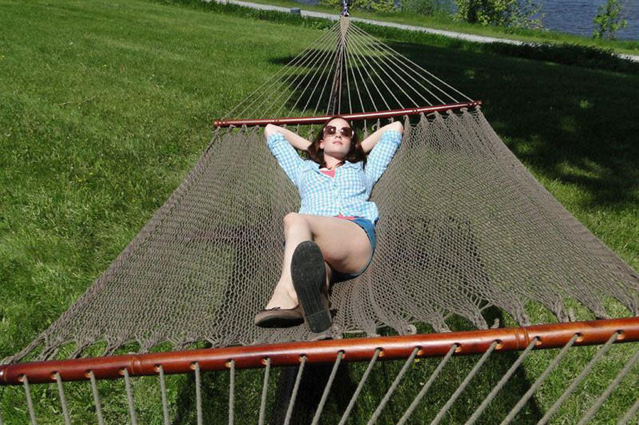 A woman with sunglasses on laying in a polyester rope hammock on a sunny day.