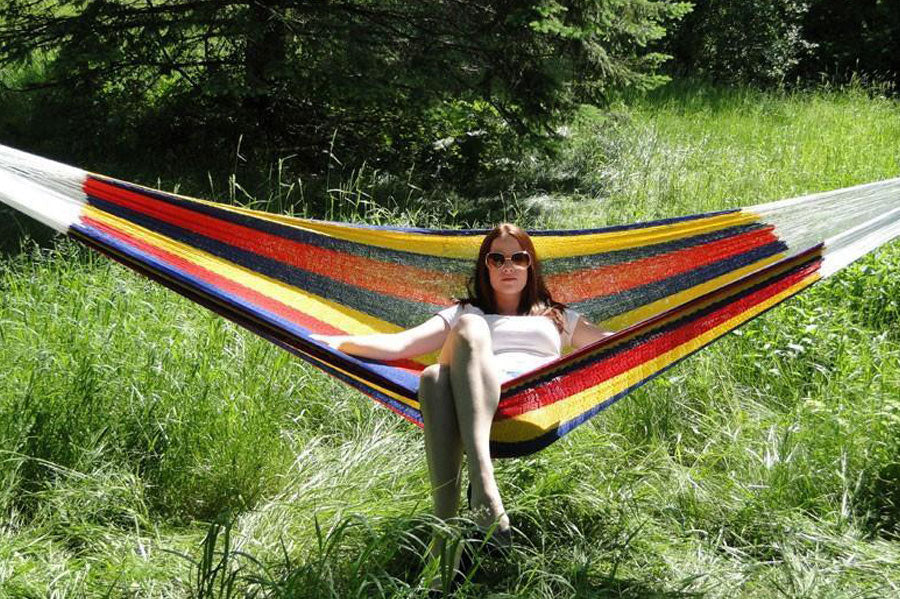 Woman with sunglasses lounging in a Mayan hammock on a sunny day.