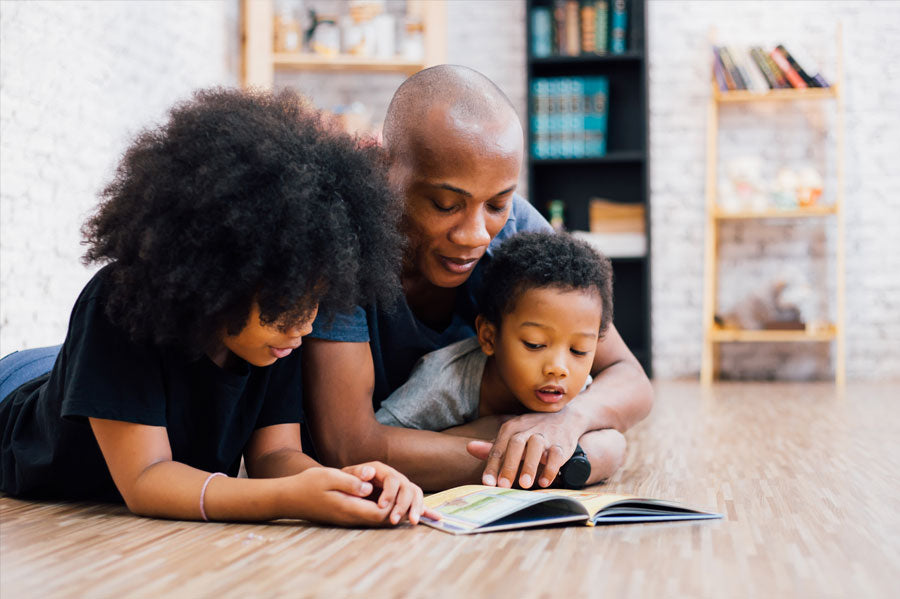 Parents reading with their child on the living room floor.