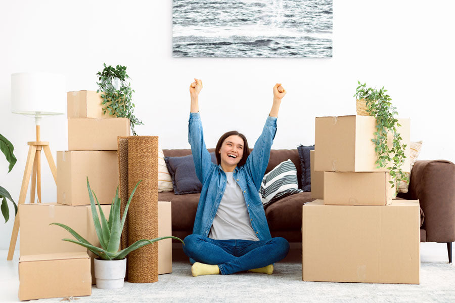 Excited young woman sitting in front of a couch surrounded by unpacked boxes