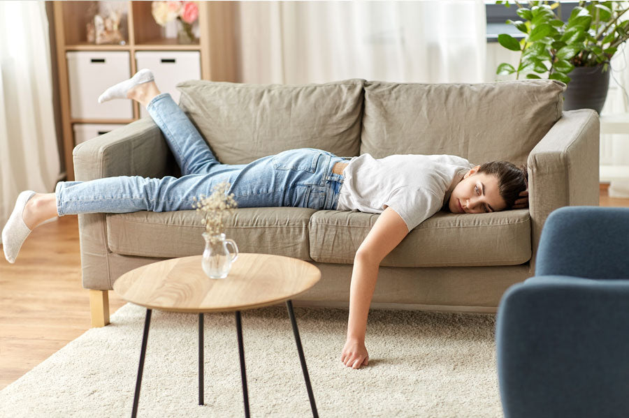 A woman laying face down on a couch in a living room, looking bored.