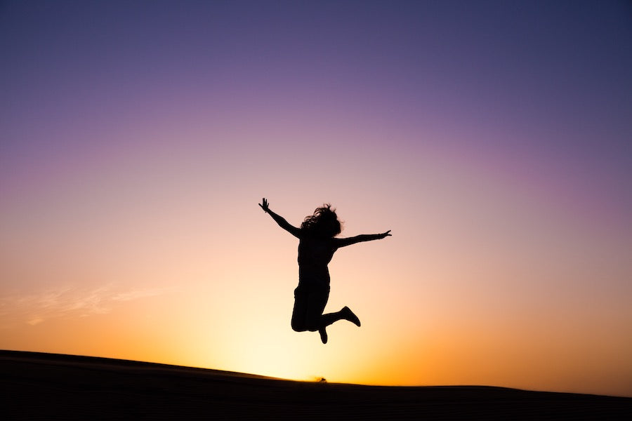 The silhouette of a woman jumping for joy at sunset.