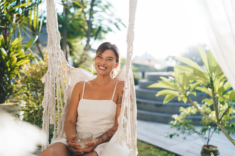 A smiling woman sitting in a rope hanging chair on a sunny day.