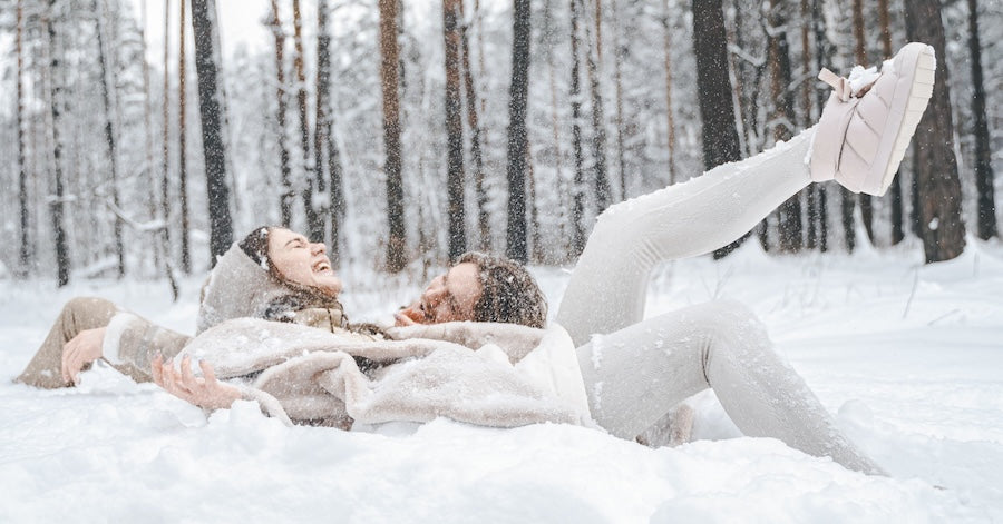 .Young couple guy girl lying,playing in snowy winter forest with trees.Walking, having fun, laughing in stylish warm clothes, concept of downtime and spending time outdoors