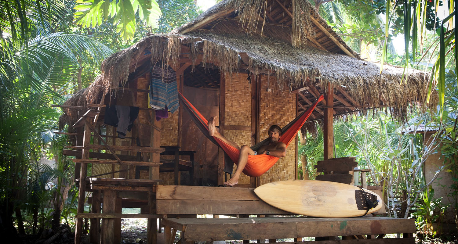 Small home in the forest with a man resting in his hammock on the porch