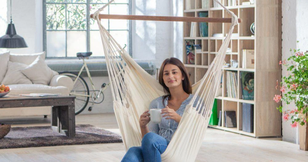 A woman enjoying a hot beverage while sitting in a Colombian hammock chair in her living room.