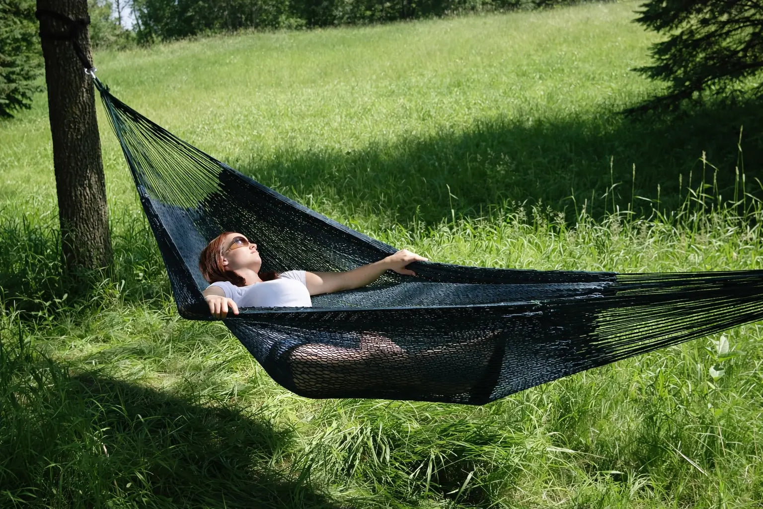 Person relaxing in a black hammock in a grassy outdoor setting #24-MHXLTC-FG