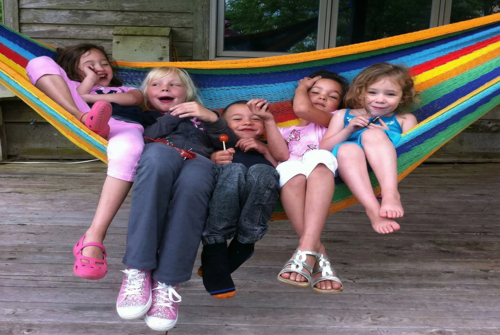 Children sitting in a colorful hammock on a wooden deck #24-MHXLTC-H