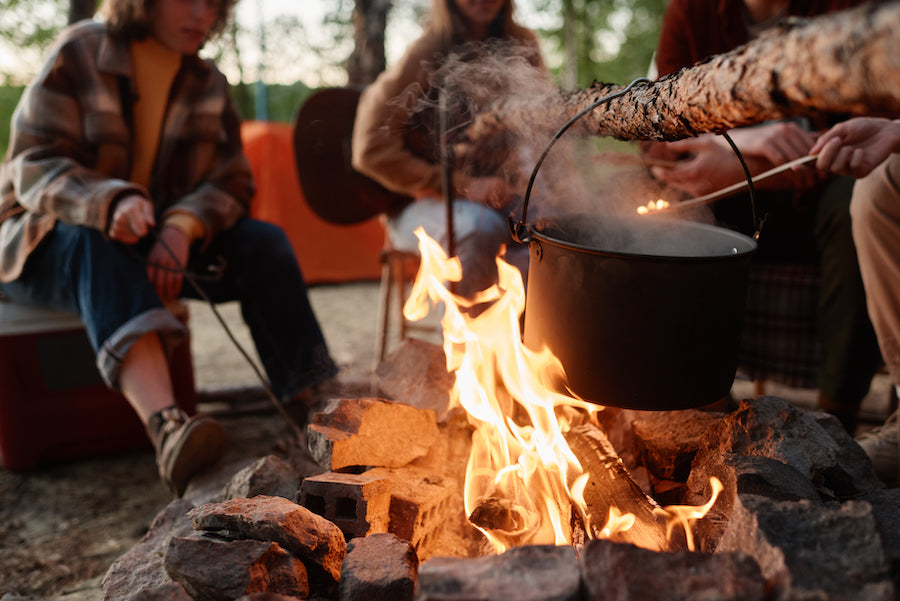 A pot hung over a campfire with two people sat around it.