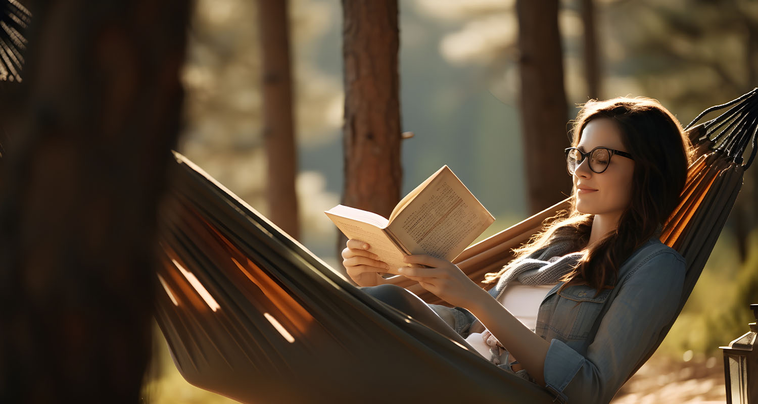 Relaxed young woman reading book while lying in hammock outdoor on sunny day