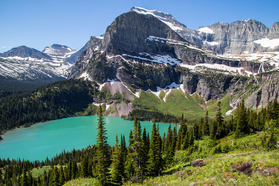 View of the Glacier National Park where you can see a forest, a blue lake and mountains in the background.