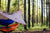 A blue hammock hanging over an orange hammock covered by a hammock tarp on a forest.