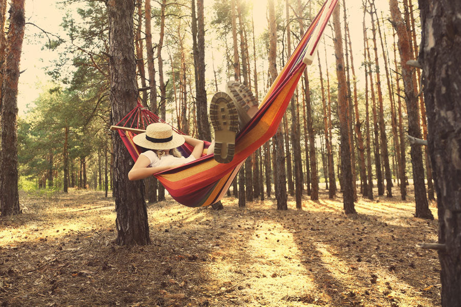 Woman with a hat covering her face sleeping in a hammock in the woods at sunset. 