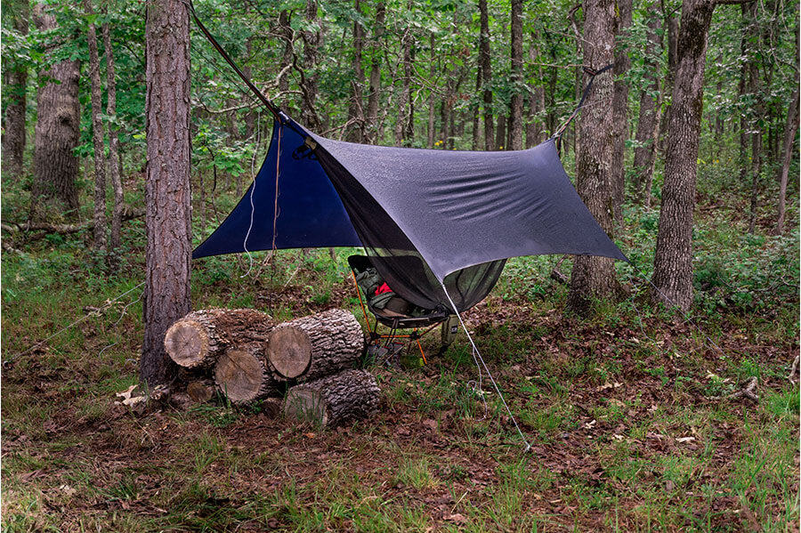 A fully set-up camping hammock with a protective cover, designed to withstand all elements for a comfortable outdoor experience.