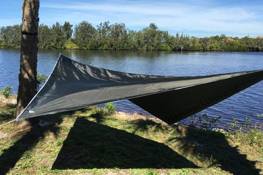 A hammock tarp attached to a tree in front of a sunny lake.