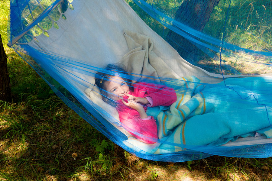 Little girl smiling in a hammock covered by a mosquito mesh net.