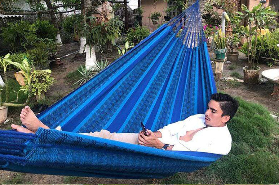 A man looking at his phone in a deluxe brazilian-style double hammock.