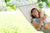 A smiling woman looking up, holding a drink in her hand and lounging in a hammock.