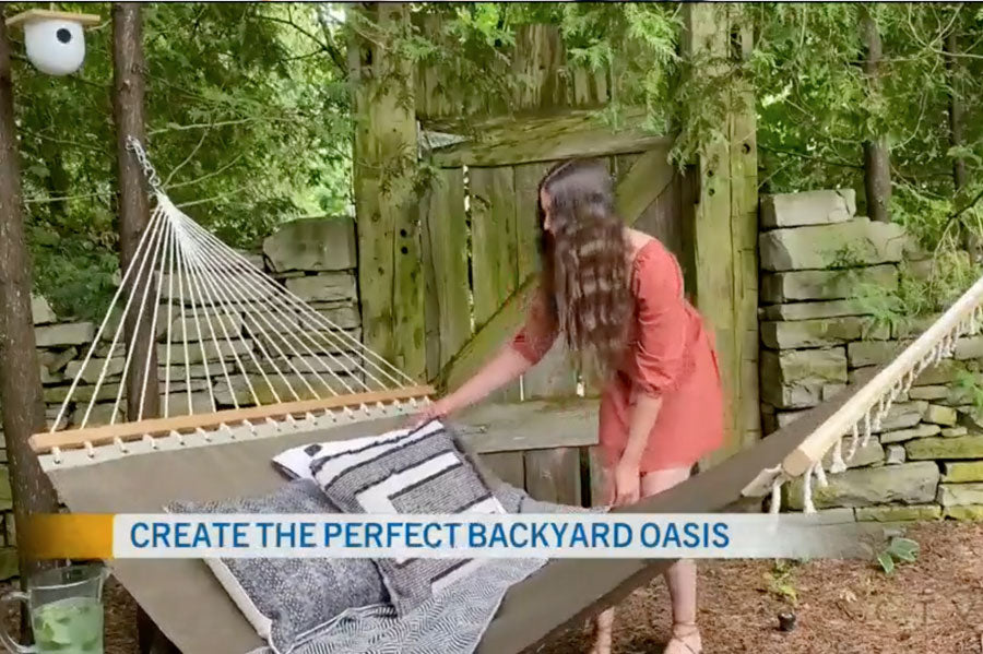 A woman arranging pillows on a hammock on a backyard with the text "Create the perfect backyard oasis" overlaid on the image.