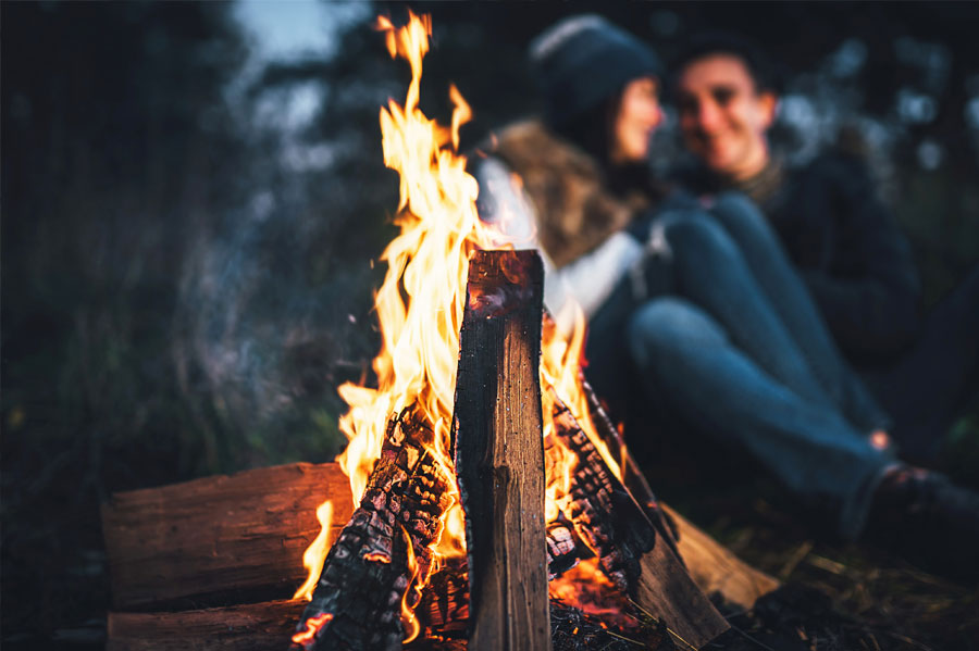 Man and woman sitting behind a campfire.