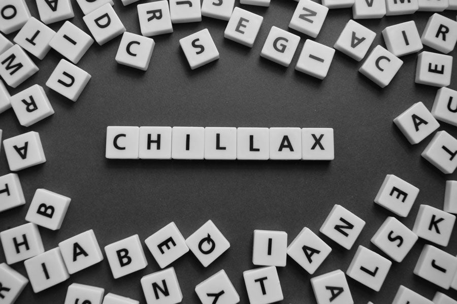 The word "chillax" spelt in scrabble letters surrounded by random scrabble tiles on a grey background.
