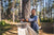 A hiker secures a hammock to a sturdy tree in a wooded area, preparing for a relaxing outdoor experience.