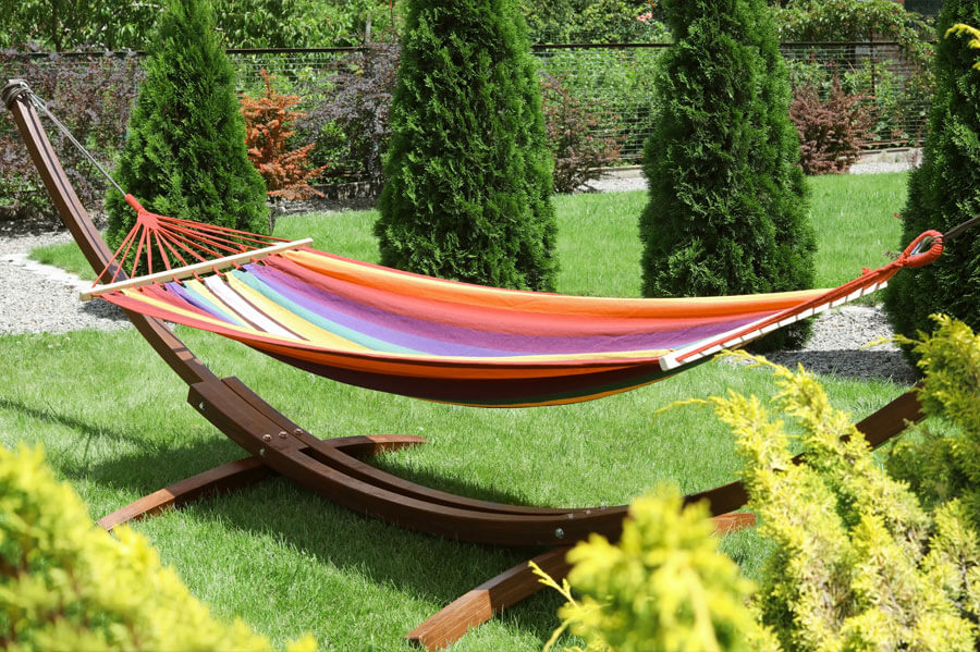 Multi-colored quilted hammock with bamboo stand in a beautiful sunny backyard