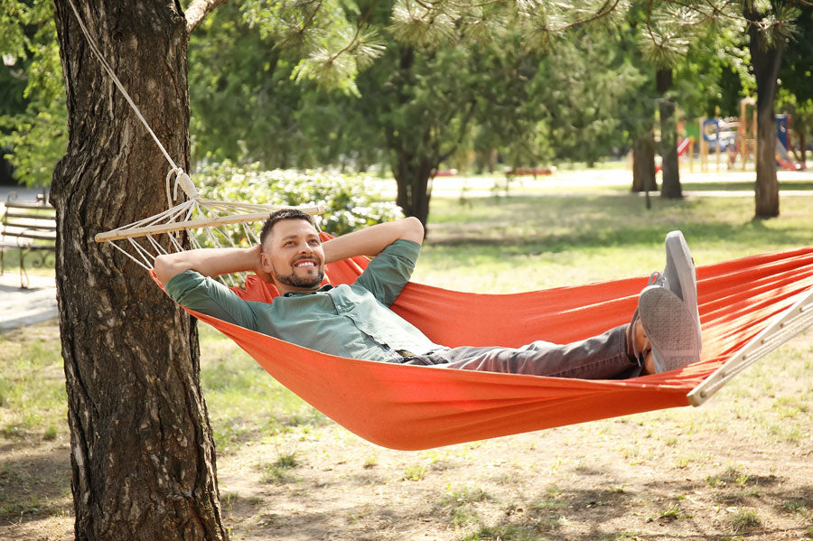 A smiling man in a hammock outdoors in a park 