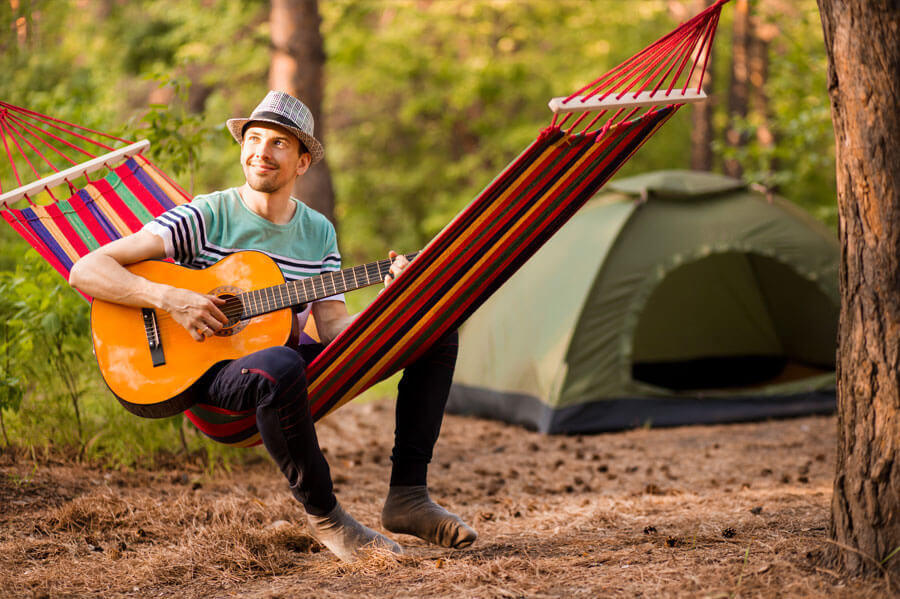 Joyful Man playing his guitar on a hammock while camping in the woods 