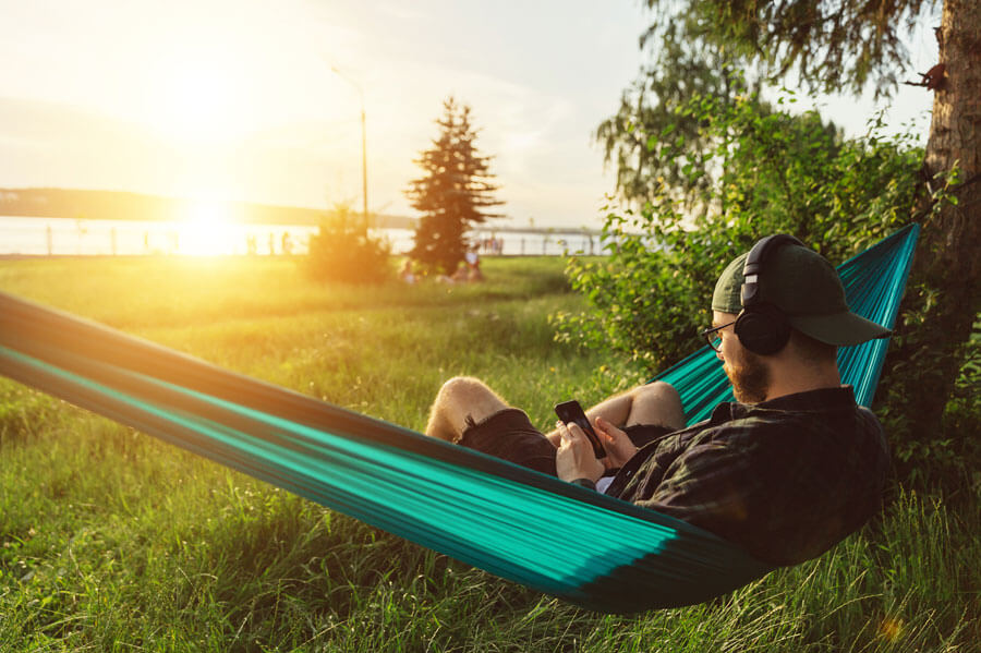 Man sitting in a hammock listening to music in the park as he enjoys a break and watching the sunset