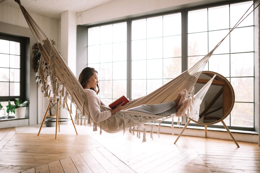 A woman reading a book while lounging in a hammock in her home.