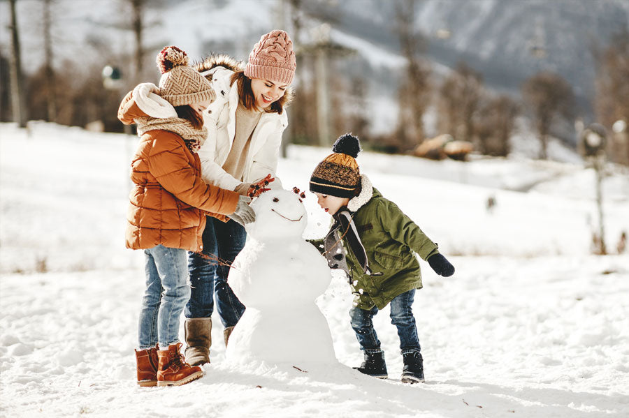 A mother and her two children building a snowman in a park.