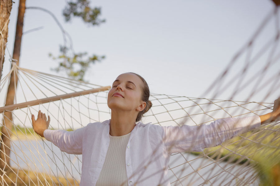 Smiling woman sitting in a hammock with her eyes closed at dawn.