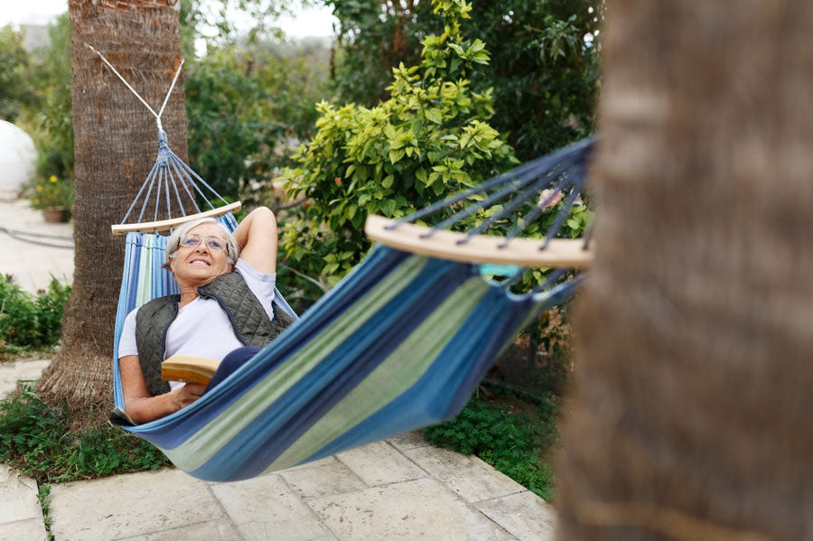 Elderly woman smiling and laying in a hammock in her backyard.