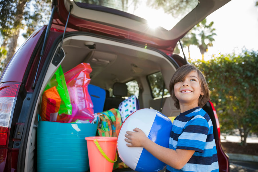Little boy putting a beachball in a packed car.