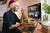 A smiling man wearing a Santa hat waiving at his coworkers on his computer.