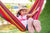 Little girl smiling on a rainbow hammock in a park.