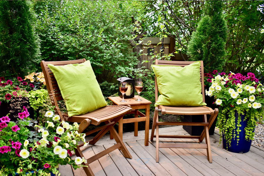 Two garden chairs with green cushions surrounded by plants and flowers