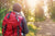 A woman walking down a trail in a sunlit forest.