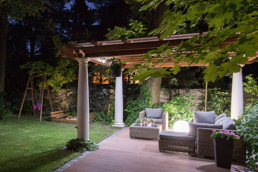 Backyard pergola with hanging lights and a grey couch at night.