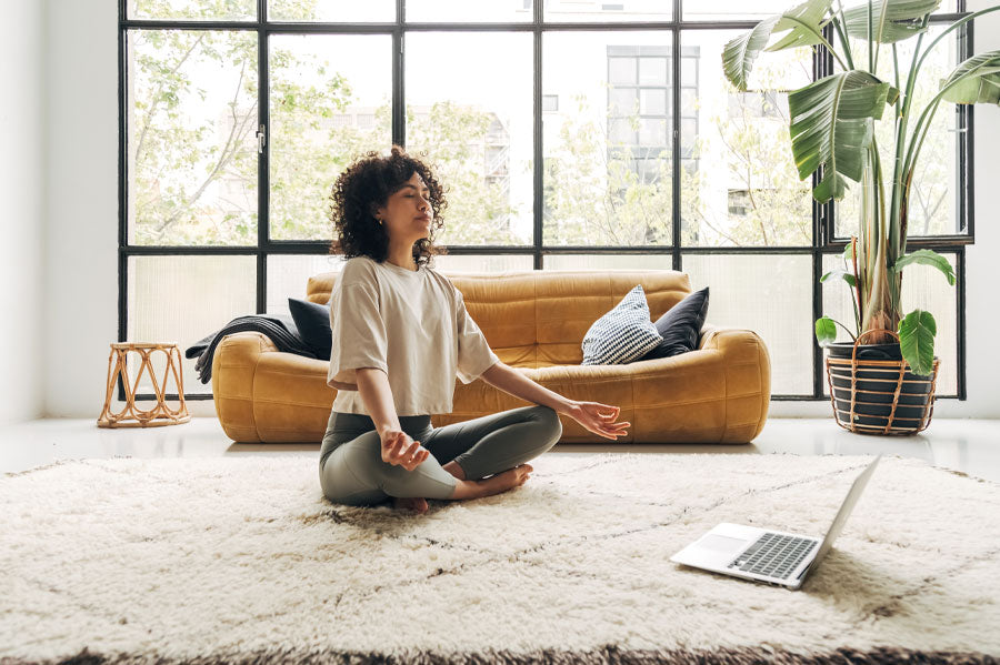 A woman meditation in front of her laptop, in a modern living room.