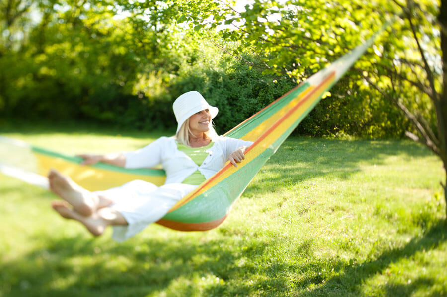 Women siting in her hammock smiling having a gentle swing in her sunny backyard