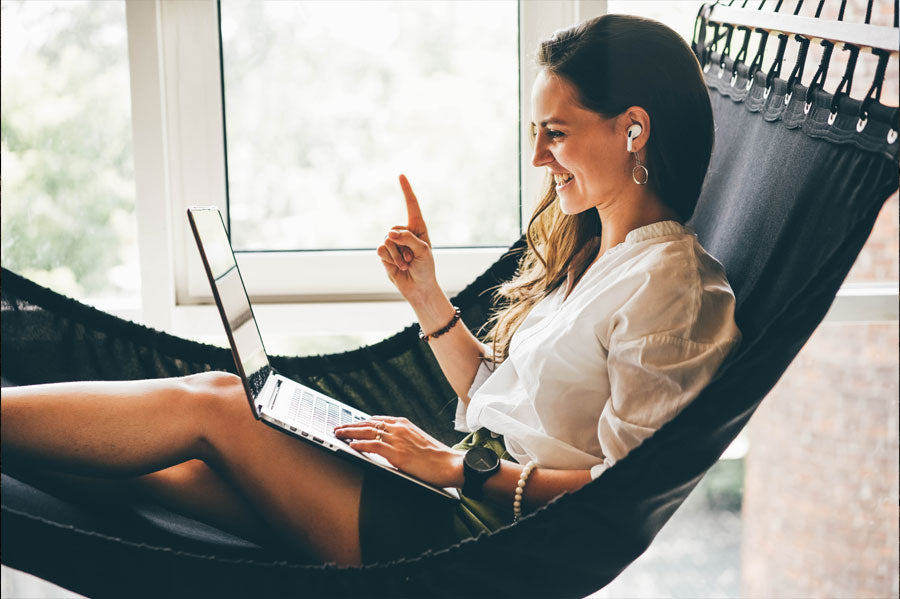 Smiling women working on her laptop in an indoor hammock