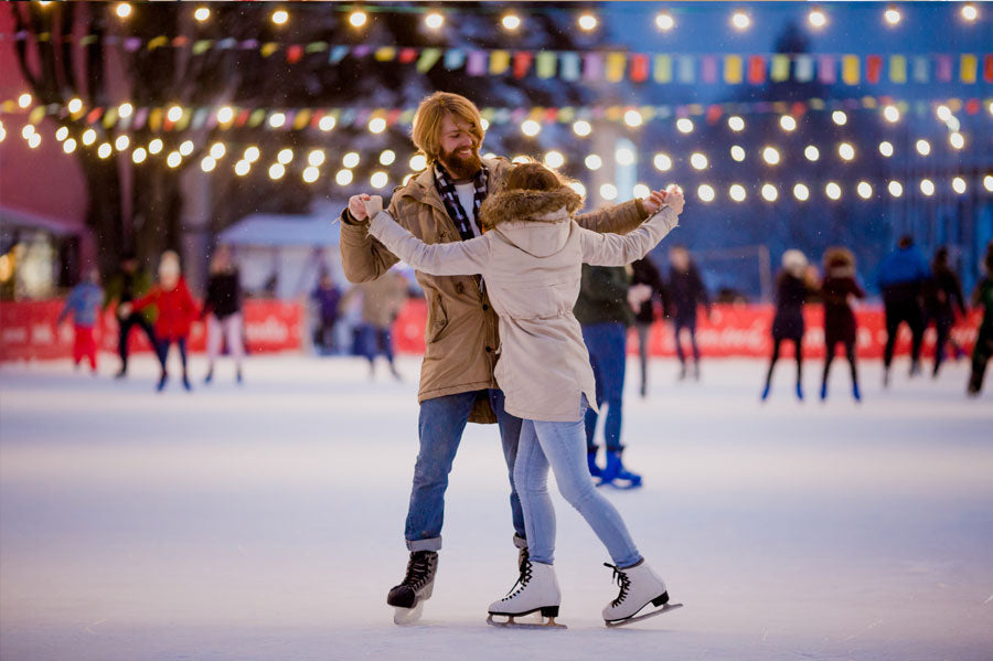 A couple skating in a well lit ice rink at night.