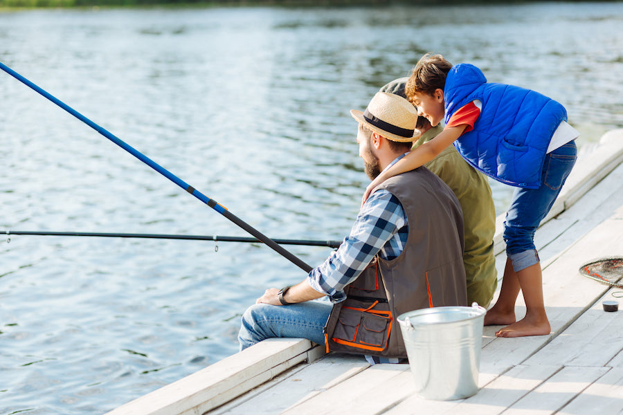 Two men fishing on a pier with a young boys arms wrapped around their shoulders.
