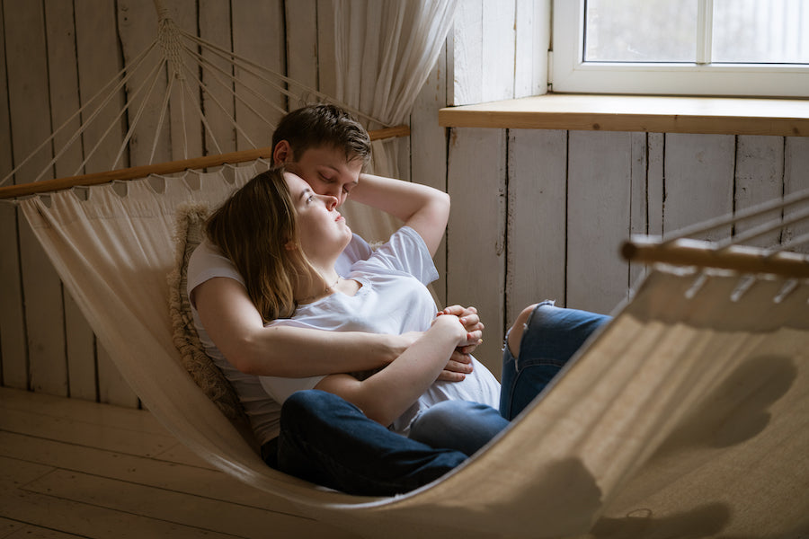 A couple cuddling on a hammock in their home.