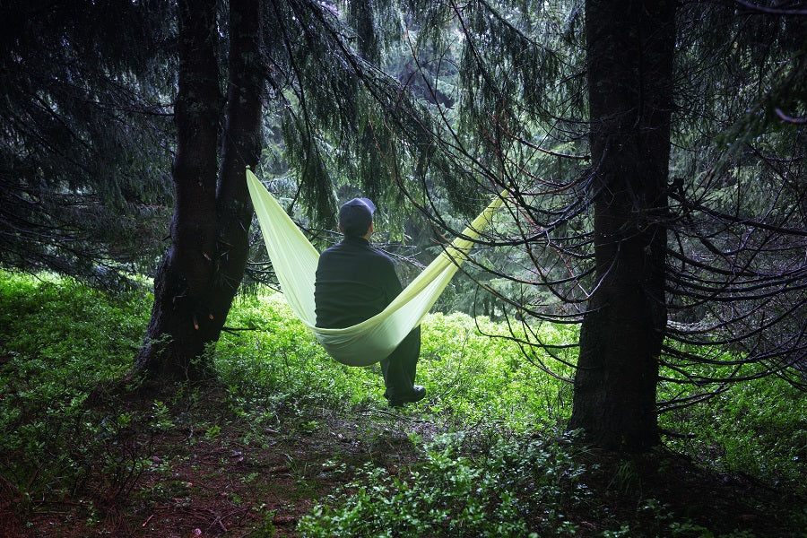 A person in a hammock in the woods on a cloudy day looking away.