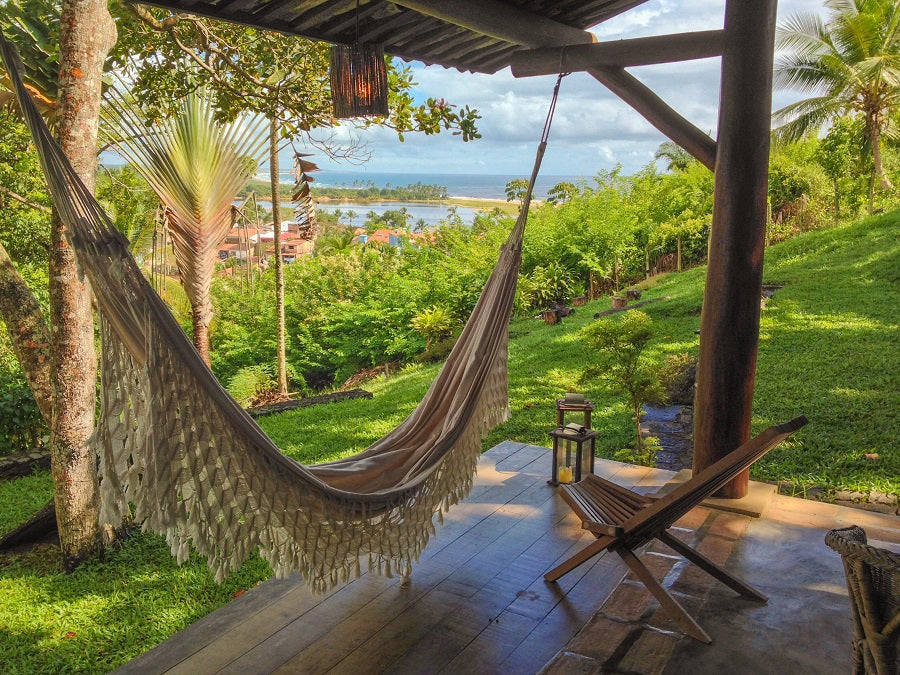 A hammock hanging under a gazebo in a sunny backyard with an ocean view.