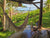 A hammock hanging under a gazebo in a sunny backyard with an ocean view.